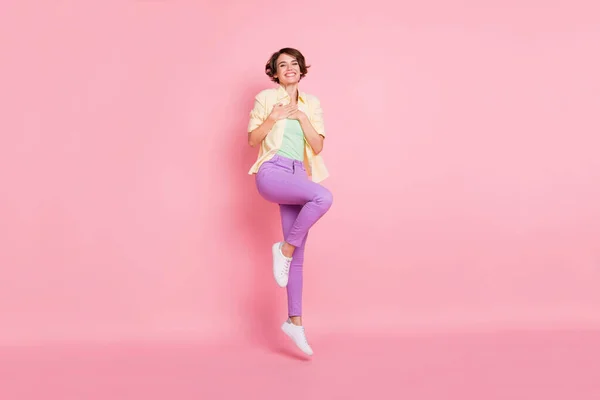Full size φωτογραφία της αισιόδοξης μελαχρινή κυρία άλμα χέρια στήθος φορούν παντελόνι πουκάμισο sneakers απομονώνονται σε παστέλ ροζ χρώμα φόντο — Φωτογραφία Αρχείου