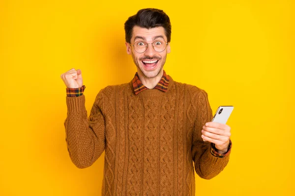 Foto di stupito eccitato giovane uomo alzare mano pugno vincere notifiche smartphone isolato su sfondo di colore giallo — Foto Stock