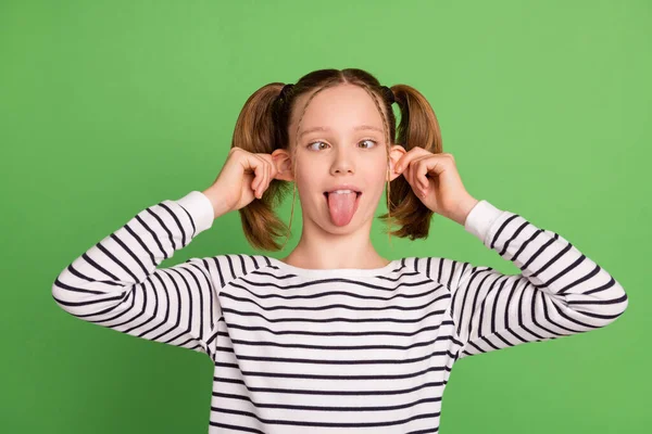 Foto di carino infantile piccola studentessa vestita maglione a righe che mostra lingua grandi orecchie cercando naso isolato colore verde sfondo — Foto Stock
