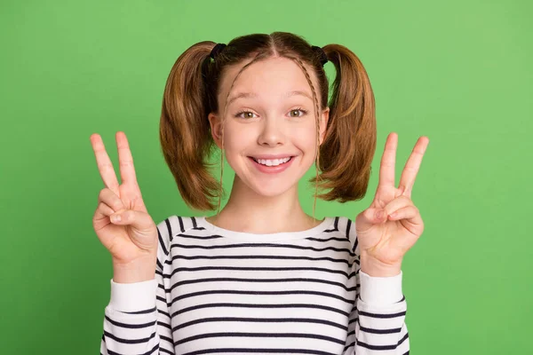 Фото смішних хвостиків зачіски маленька дівчинка показує v-знак одягнений смугастий светр ізольований на фоні зеленого кольору — стокове фото