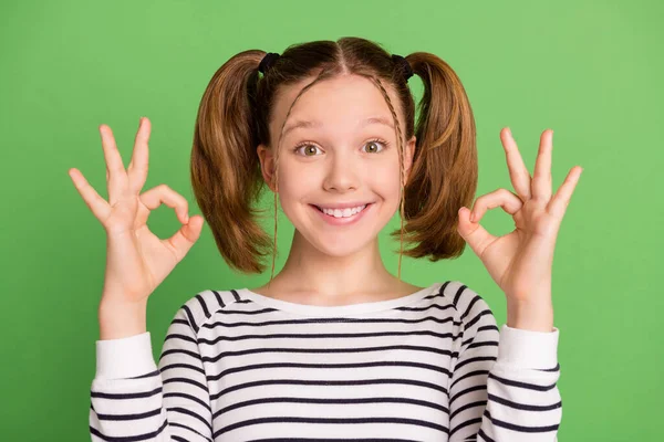 Foto de dulce encantadora niña de la escuela usar jersey blanco sonriendo mostrando signos okey aislado fondo de color verde —  Fotos de Stock