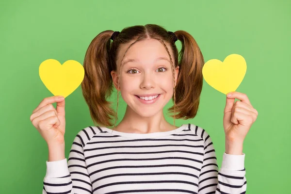 Foto de bonito adorável menina da escola usar pulôver branco sorrindo segurando dois corações de papel isolado fundo cor verde — Fotografia de Stock