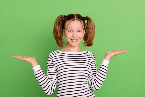 Φωτογραφία από όμορφη ξανθιά hairdo μικρό κορίτσι κατέχουν κενό χώρο φορούν ριγέ πουλόβερ που απομονώνονται σε πράσινο χρώμα φόντο — Φωτογραφία Αρχείου