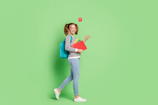 Foto di affascinante giocoso piccola studentessa vestita a strisce maglione zaino camminare gettando giocattolo isolato colore verde sfondo — Foto Stock