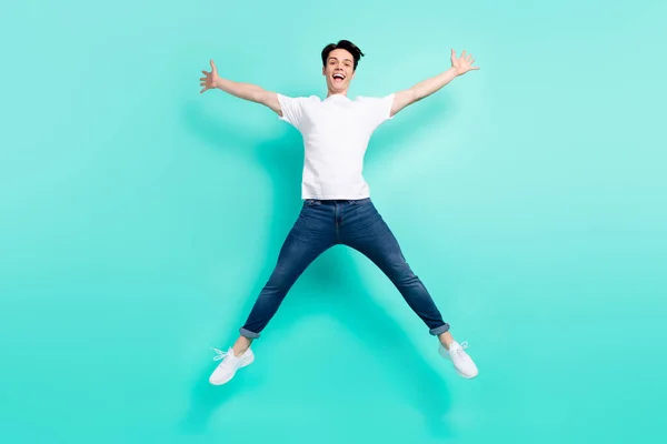 Full body photo of funky brunet hairdo teen guy jump wear t-shirt jeans isolated on teal background — Stock Photo, Image