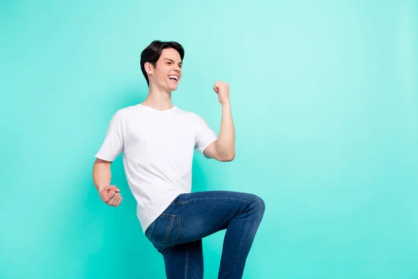 Foto retrato jovem cara em branco t-shirt sorrindo overjoyed gestos como vencedor isolado brilhante teal cor de fundo — Fotografia de Stock