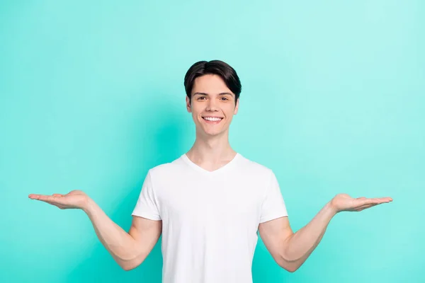 Foto van funky brunet kapsel tiener jongen houden lege ruimte dragen witte t-shirt geïsoleerd op levendige teal kleur achtergrond — Stockfoto