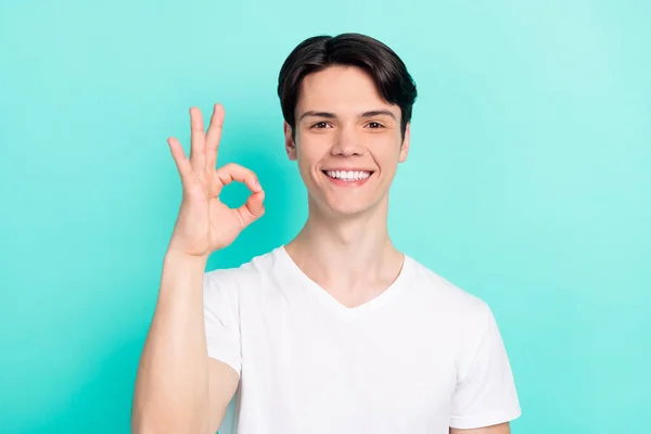 Foto van grappig brunet kapsel tiener guy show okey teken dragen wit t-shirt geïsoleerd op levendige teal kleur achtergrond — Stockfoto