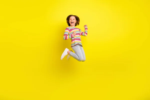 Full storlek profil foto av hurra kort frisyr liten flicka hoppa händer nävar bära skjorta byxor sneakers isolerade på gul färg bakgrund — Stockfoto