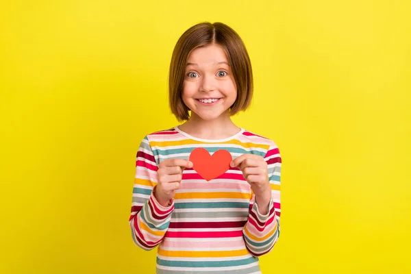 Foto de atraente feliz jovem menina segurar as mãos pequeno papel vermelho figura do coração isolado no fundo de cor amarela — Fotografia de Stock