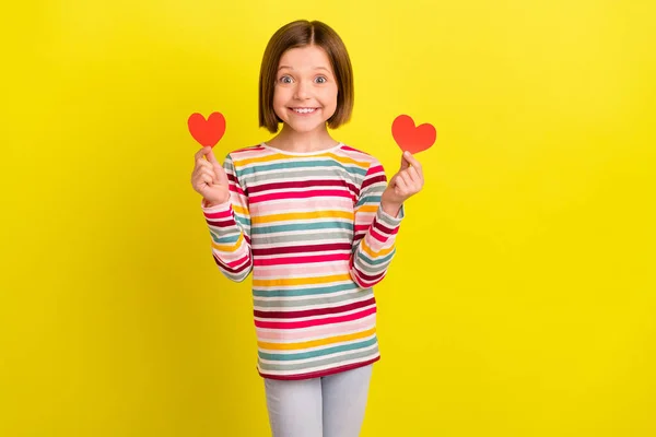 Foto de penteado curto bonito menina pequena segurar corações usar camisa colorida isolada no fundo de cor amarelo vívido — Fotografia de Stock