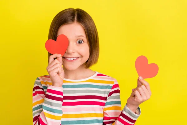 Foto retrato menina mantendo dois pequenos cartões postais do coração sorrindo cobertura olho isolado cor amarela brilhante fundo — Fotografia de Stock