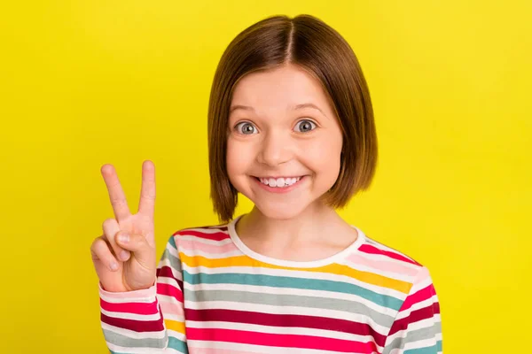 Foto retrato niña mostrando gesto v-signo sonriendo aislado color amarillo brillante fondo —  Fotos de Stock