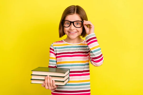 Foto retrato niña asombrada con gafas camisa rayada mantener pila libro aislado color amarillo brillante fondo —  Fotos de Stock