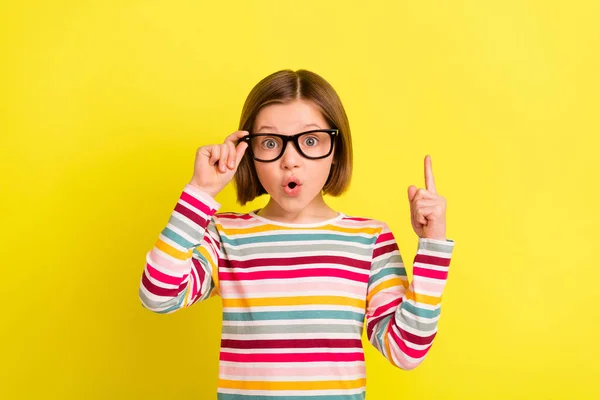 Foto van verbaasd geschokt klein meisje wijzen vinger omhoog idee slimme slijtage bril geïsoleerd op gele kleur achtergrond — Stockfoto