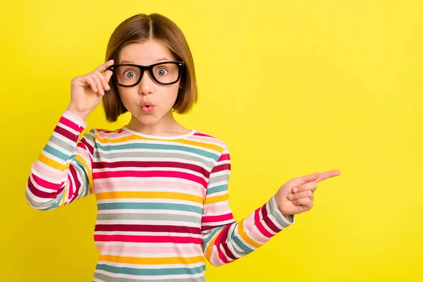 Foto retrato niña asombrada apuntando copyspace con el dedo en gafas aisladas de color amarillo vibrante fondo —  Fotos de Stock