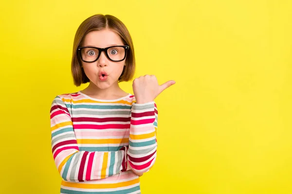 Foto von erstaunt schockiert kleine Mädchen Zeigefinger leer Raum tragen Gläser isoliert auf gelbem Hintergrund — Stockfoto