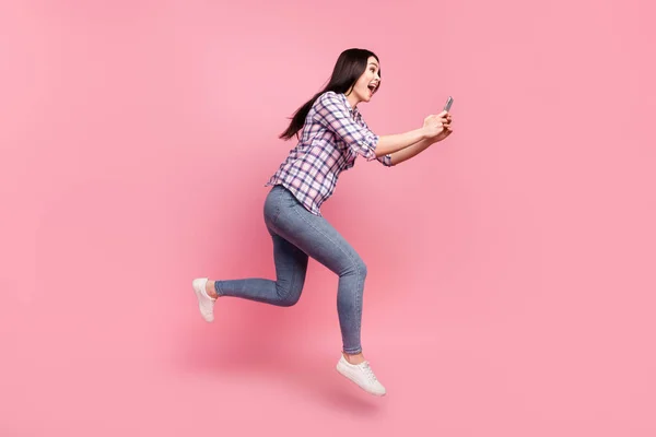 Foto de longitud completa de linda señora joven vestida camisa a cuadros mecanografía gadget moderno saltar alto aislado color rosa fondo — Foto de Stock