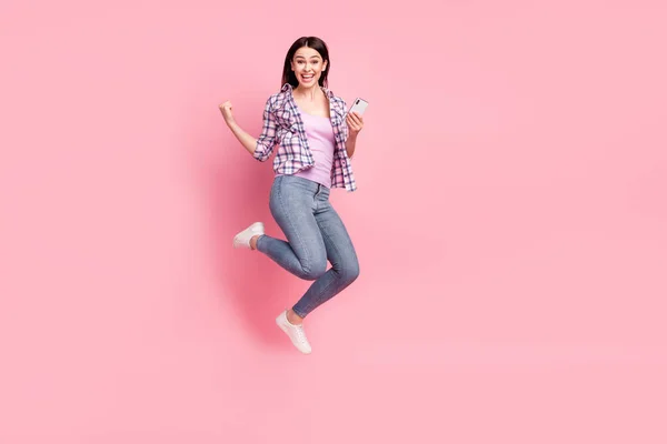Повна довжина тіла фото дівчини в картатій сорочці, що тримає жест мобільного телефону, як переможець, ізольований пастельно-рожевий кольоровий фон — стокове фото