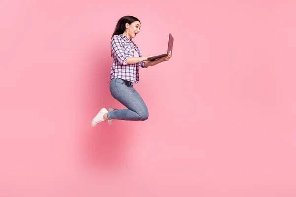 Tamanho do corpo de comprimento total vista de linda menina alegre maravilhado pulando usando laptop isolado sobre cor pastel rosa fundo — Fotografia de Stock