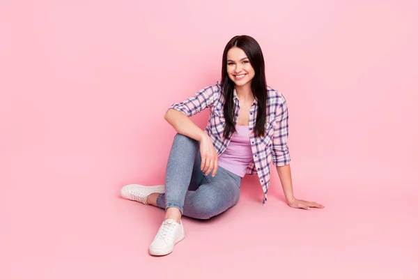 Foto em tamanho completo de doce jovem senhora sentar desgaste xadrez camisa jeans tênis isolado no fundo cor-de-rosa — Fotografia de Stock