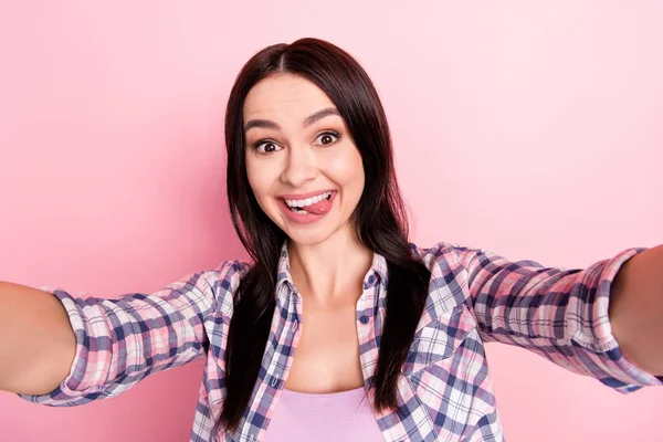 Photo of charming cute young lady dressed plaid shirt smiling showing tongue tacking selfie isolated pink color background — Stock Photo, Image