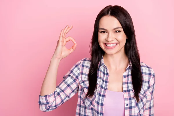 Foto de bastante brillante joven dama vestida camisa a cuadros que muestra signo okey sonriendo aislado color rosa fondo — Foto de Stock