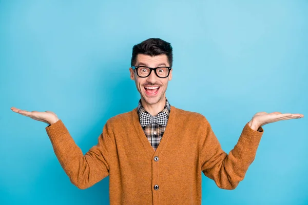 Foto van brunette jongeman houd handen leeg ruimte dragen geruite strik bril geïsoleerd op blauwe kleur achtergrond — Stockfoto