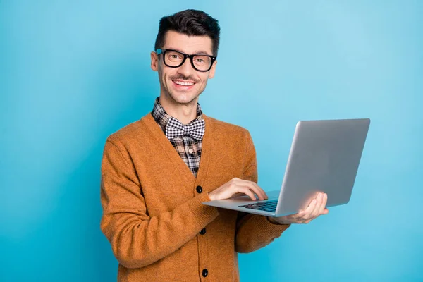 Фото позитивного хорошого молодого хлопця, одягненого в коричневий кардиган, що друкує сучасний пристрій ізольований синій колір фону — стокове фото