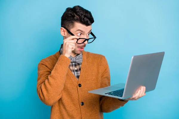 Foto van doordachte onder de indruk jonge man hand dragen bruin vest op zoek naar moderne gadget geïsoleerde blauwe kleur achtergrond — Stockfoto