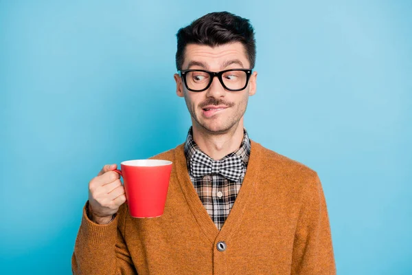 Foto de jovem sedento duvidoso usar óculos de lã marrom segurando copo vermelho isolado fundo de cor azul — Fotografia de Stock