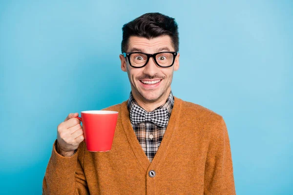 Фото позитивного веселого молодого парня одетый коричневый кардиган очки с красной чашкой изолированный синий цвет фона — стоковое фото