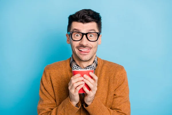 Foto von verrückten funky junger Mann halten Tasse trinken Latte Biss Zähne Zunge isoliert auf pastellblauem Hintergrund — Stockfoto