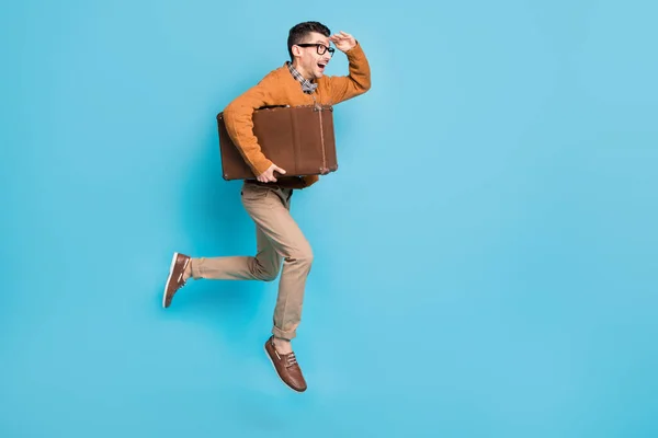 Full size profiel zijkant foto van brunette man dragen bowtie glazen kijken lege ruimte naar voren springen hold tas geïsoleerd op blauwe kleur achtergrond — Stockfoto