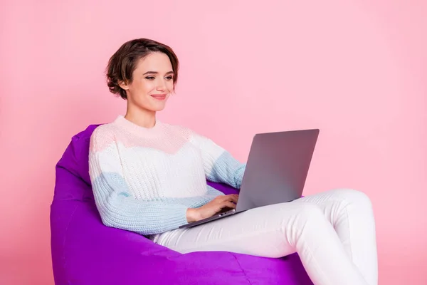 Foto portrét ženy procházející internet na notebooku sedí ve fialové beanbag židle izolované na pastelové růžové barevné pozadí — Stock fotografie