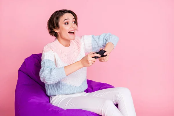 Foto portret van gamer meisje met joystick zitten in violette zitzak stoel geïsoleerd op pastel roze gekleurde achtergrond — Stockfoto