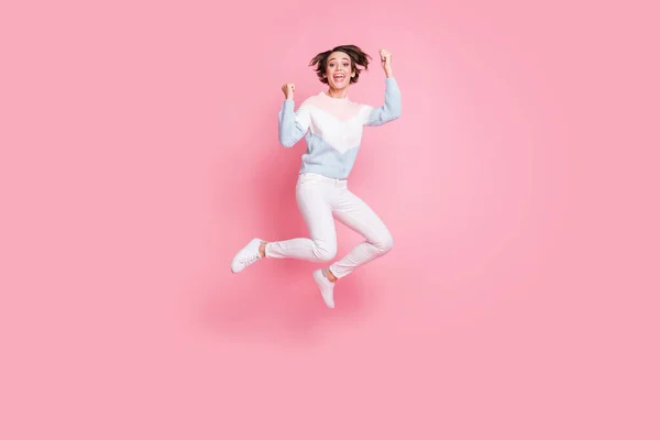 Lunghezza completa foto di funky fortunato giovane donna indossare maglione saltando pugni in aumento isolato colore rosa sfondo — Foto Stock