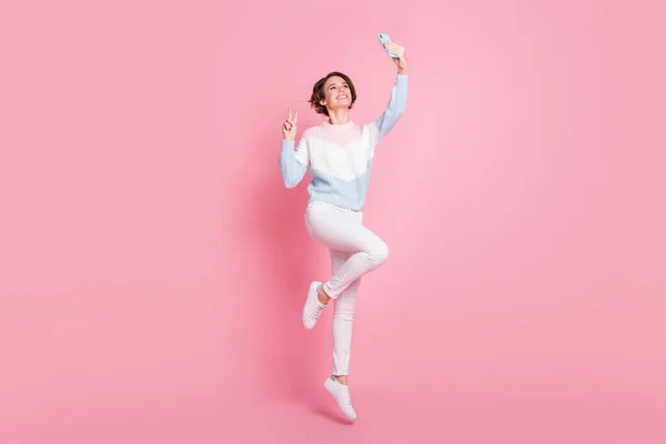 귀엽고 귀여운 젊은 여성의 전체 길 이 사진은 점프 태킹 셀카를 입고 v-sign 고립된 핑크 색 배경을 보여준다. — 스톡 사진