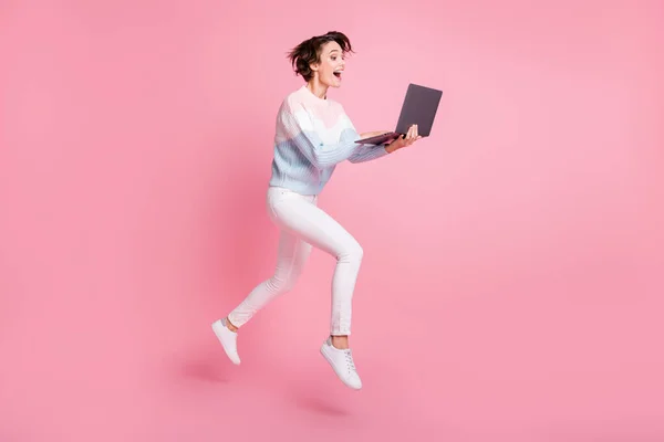 Full length φωτογραφία πορτρέτο του ενθουσιασμένοι κορίτσι με φορητό υπολογιστή άλμα επάνω απομονωμένο σε παστέλ ροζ φόντο — Φωτογραφία Αρχείου