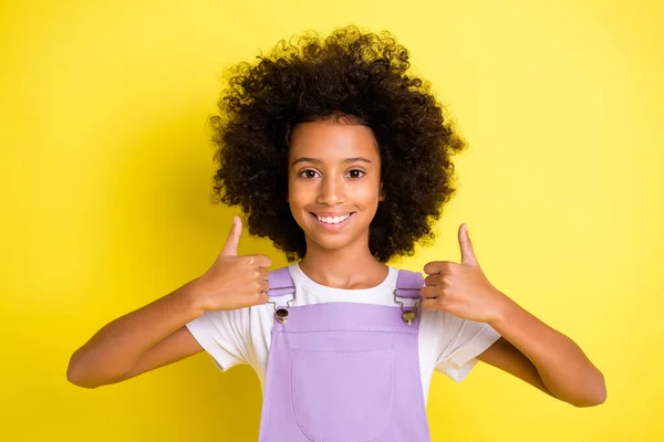 Фото положительной маленькой девочки поднять большой палец вверх смотреть камеру носить фиолетовый общий изолированный желтый цвет фона — стоковое фото