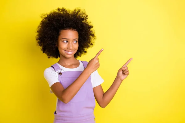 Photo of little girl indicate fingers look side empty space wear violet overall isolated yellow color background — Stock Photo, Image