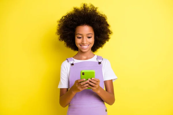 Foto de chica rizada linda optimista look teléfono desgaste camiseta blanca vestido violeta aislado sobre fondo de color amarillo — Foto de Stock