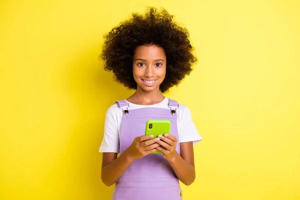 Foto de otimista bonito encaracolado menina segurar telefone desgaste branco t-shirt vestido violeta isolado no fundo cor amarela — Fotografia de Stock