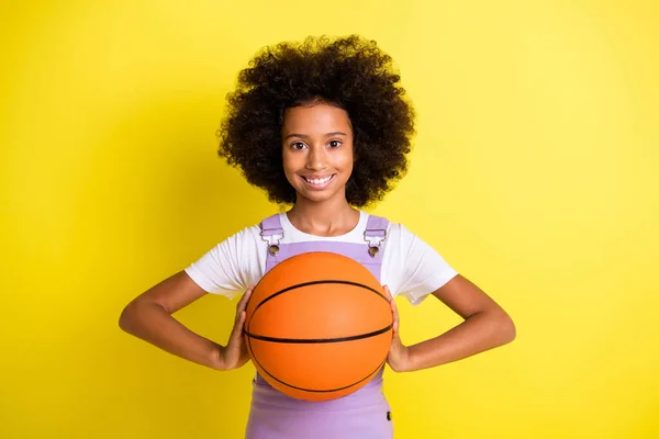 Photo of cheerful small girl hold ball beaming smile wear violet overall isolated yellow color background — Stock Photo, Image