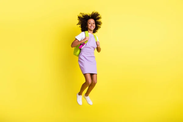 Teljes hossz testméret kilátás szép vidám hullámos hajú lány ugrás hordtáska vissza az iskolába elszigetelt felett élénk sárga háttér — Stock Fotó