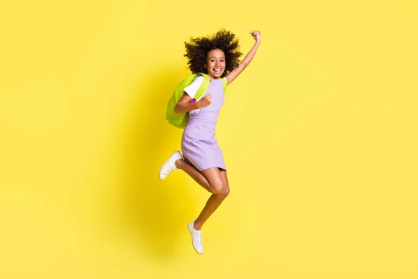 Full size foto van optimistisch schattig krullend meisje springen slijtage rugzak t-shirt jurk geïsoleerd op gele kleur achtergrond — Stockfoto