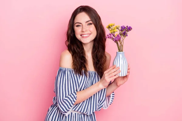 İyimser, esmer bir bayanın elinde çiçeklerle çekilmiş fotoğrafı pembe arka planda izole edilmiş mavi bir elbise giyiyor. — Stok fotoğraf