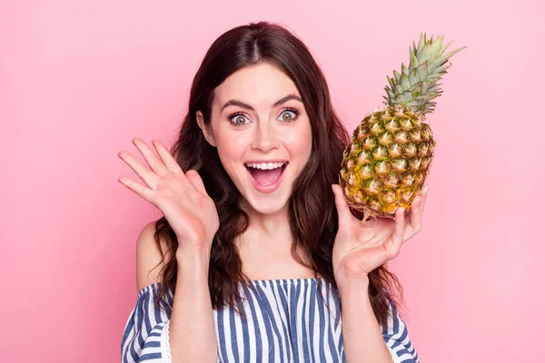 Foto de linda mujer joven impresionada vestida a rayas levantando brazos sosteniendo fruta aislado color rosa fondo —  Fotos de Stock