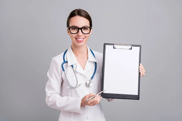Фотопортрет молодої медсестри з стетоскопом усміхнений тримаючи ручку буфера ізольований сірий кольоровий фон — стокове фото