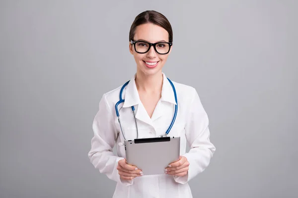 Фото впевненої позитивної молодої леді лікар робочий одяг окуляри посміхаючись набираючи сучасний гаджет ізольований сірий кольоровий фон — стокове фото